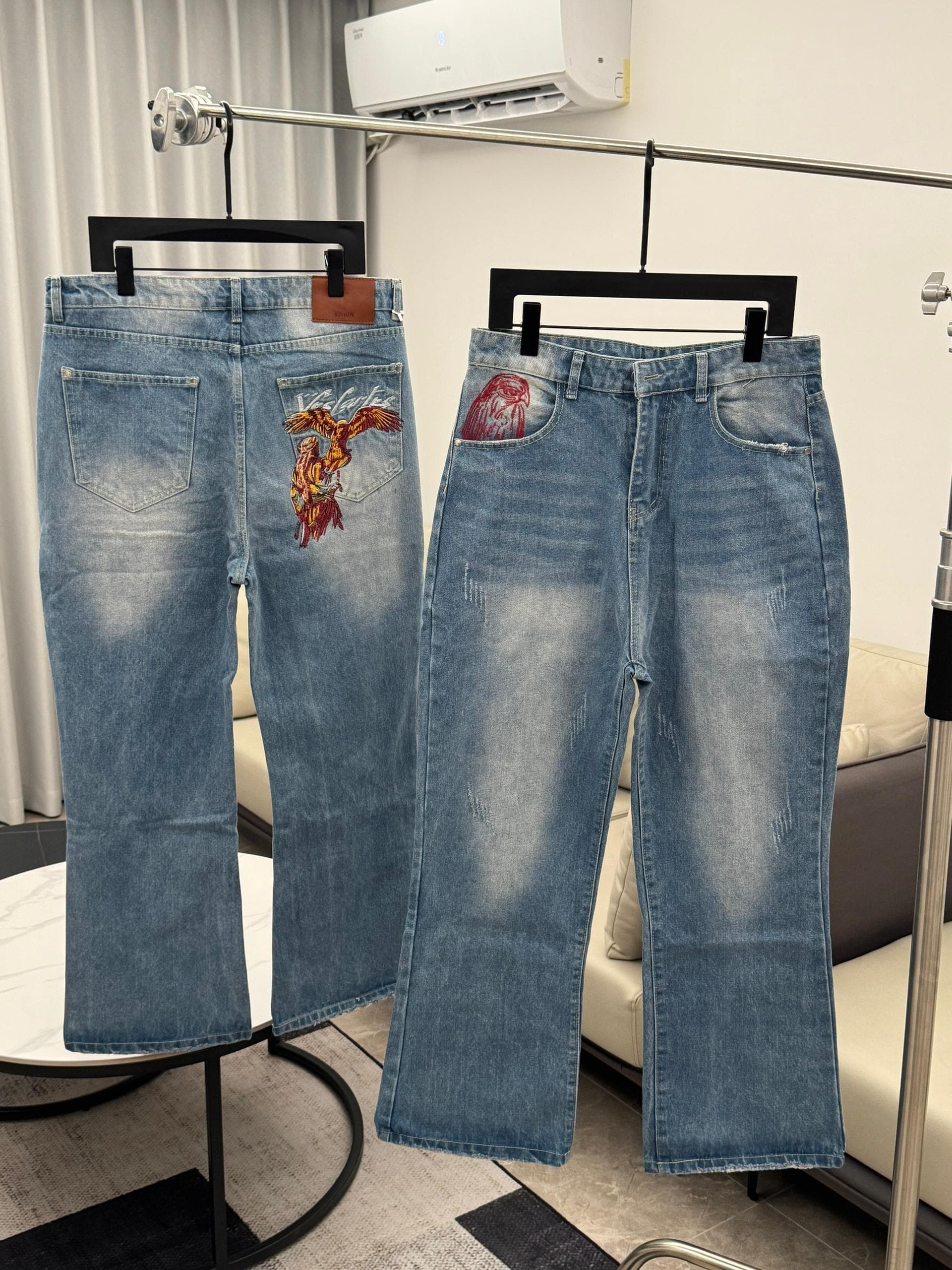 Light blue jeans with eagle embroidery on back pocket, shown hanging with another pair.