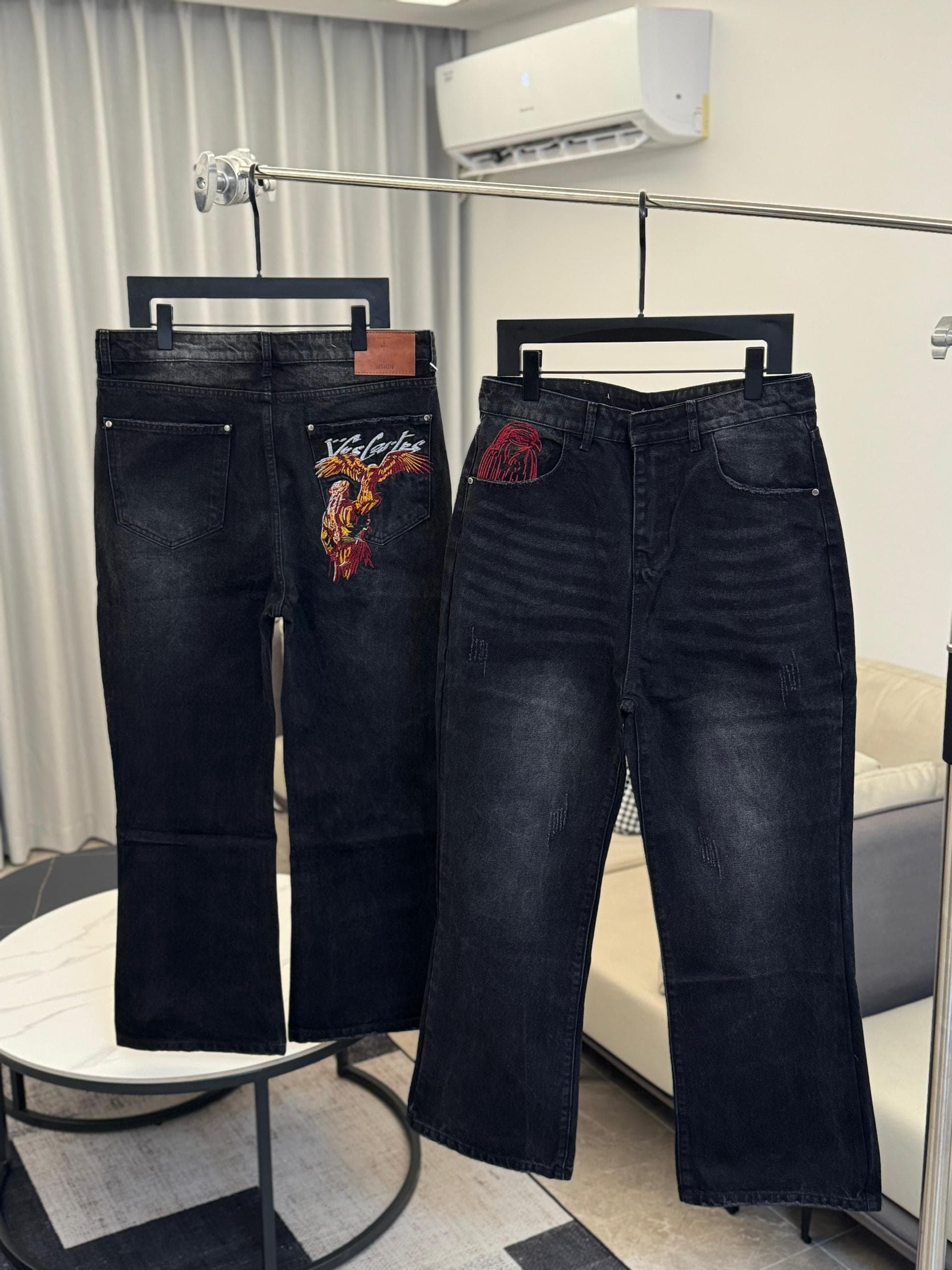 Black jeans with colorful eagle and Viscartes embroidery on back pocket, shown hanging.