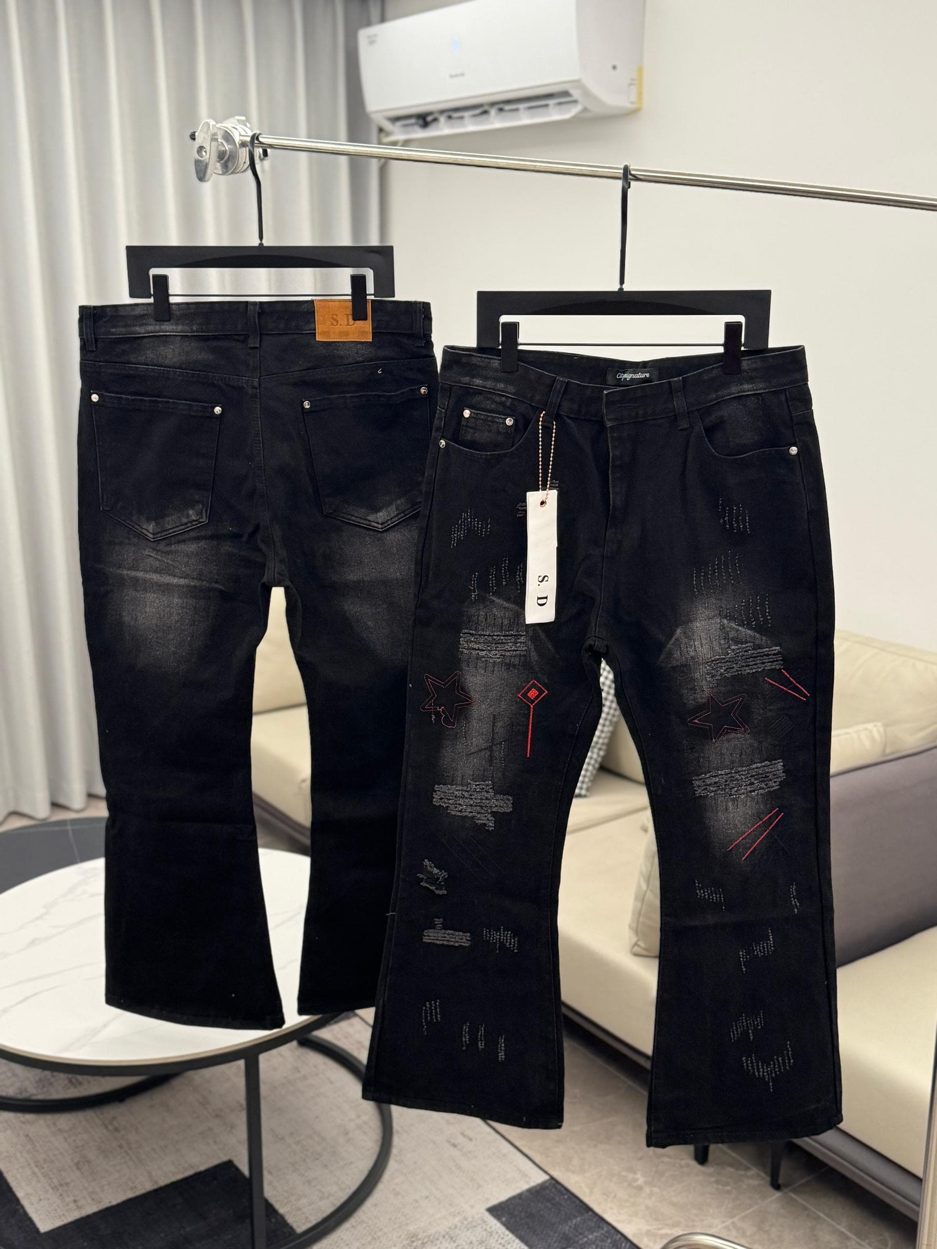 Black distressed jeans with red stitch patterns and stars, shown hanging front and back.