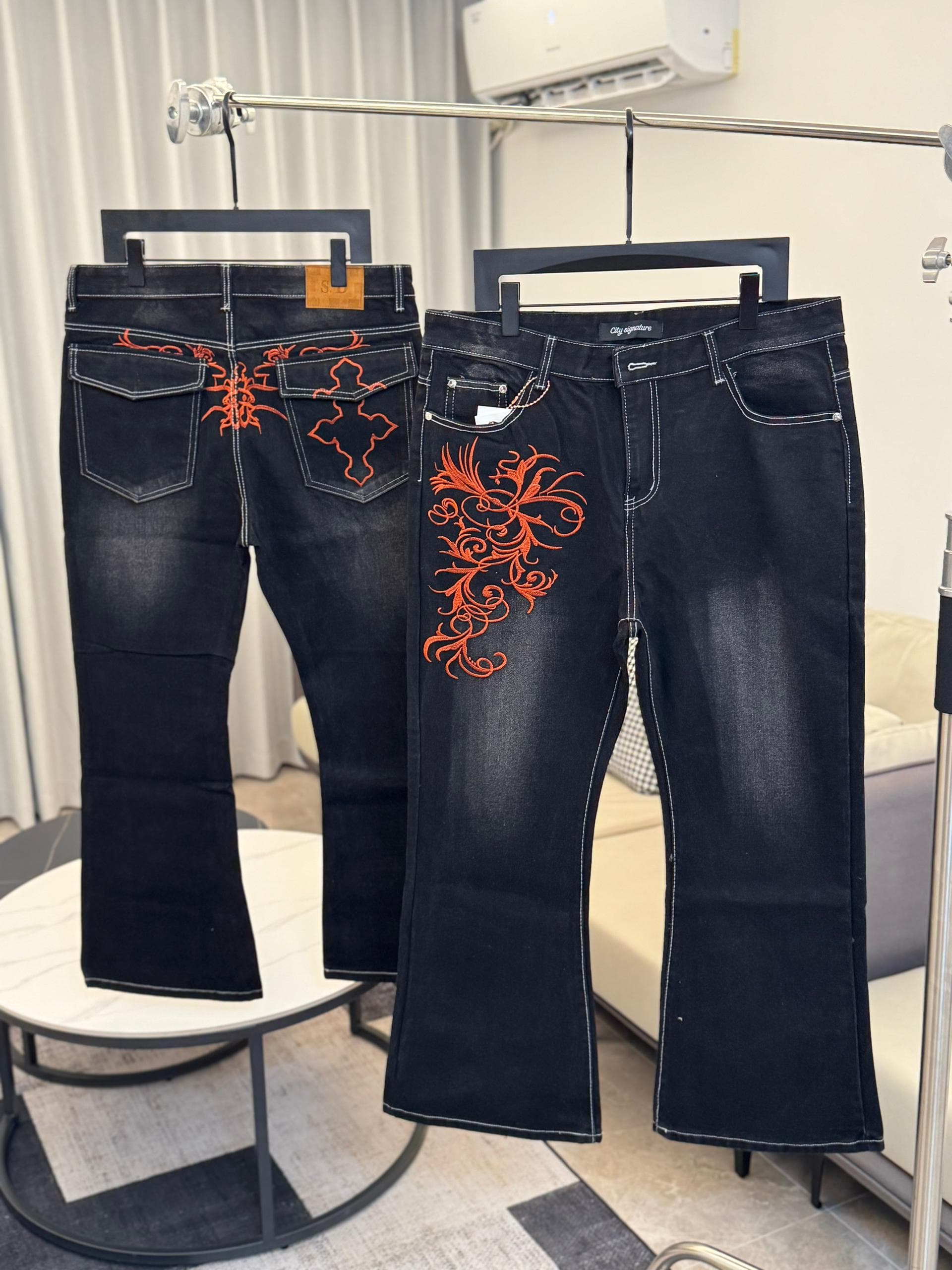 Black flared jeans with large orange swirl embroidery on the leg and pocket area.