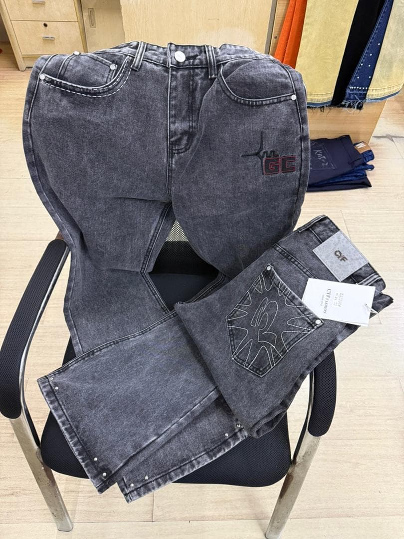 Gray jeans with GC embroidery displayed on chair alongside folded view of back pocket.
