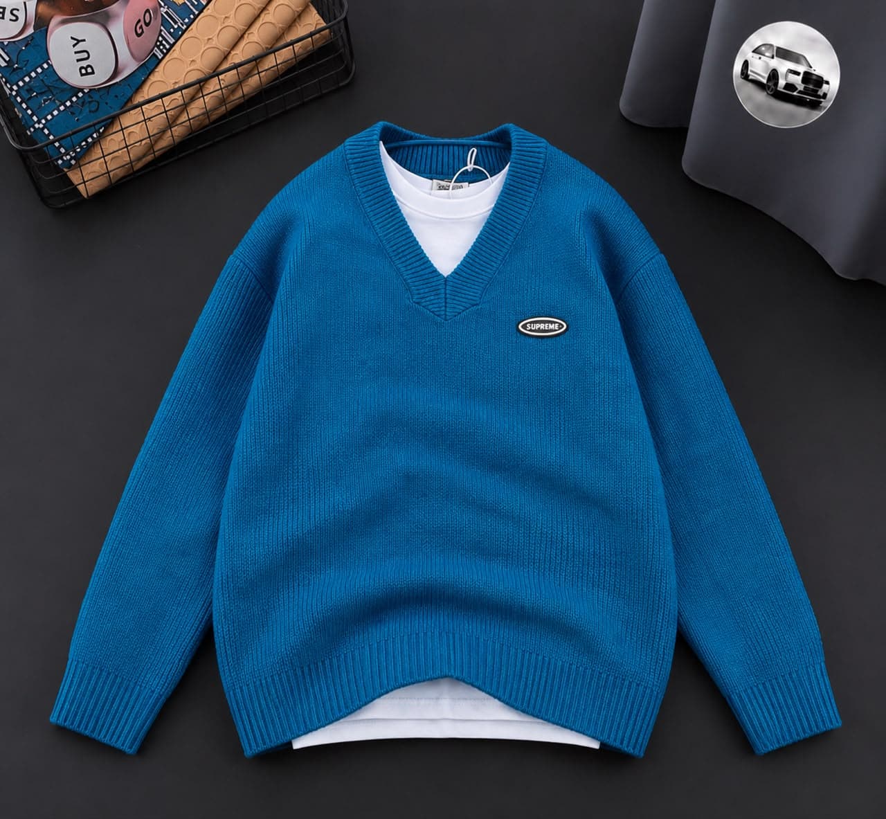 Blue V-neck sweater with Supreme logo on the chest, layered over white tee.