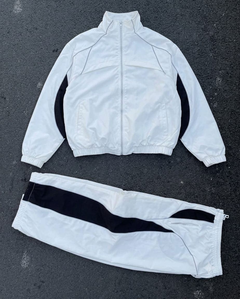 White cargo tracksuit with black contrast stripes and panels, flat lay on dark surface.