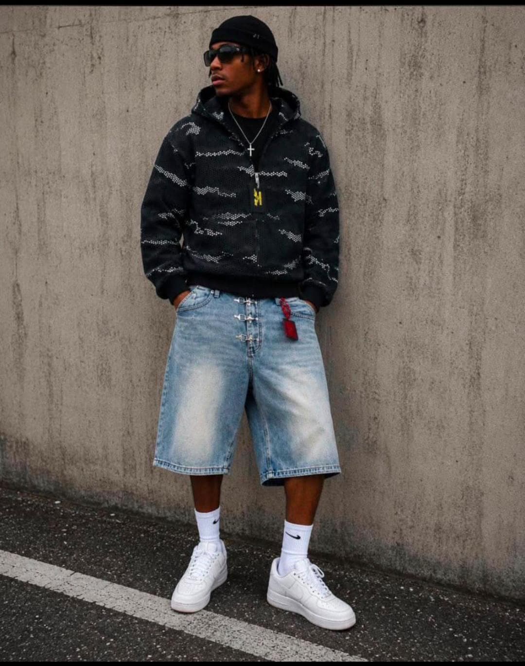 Model wearing black camo mesh zip-up hoodie with denim shorts and sneakers outdoors.