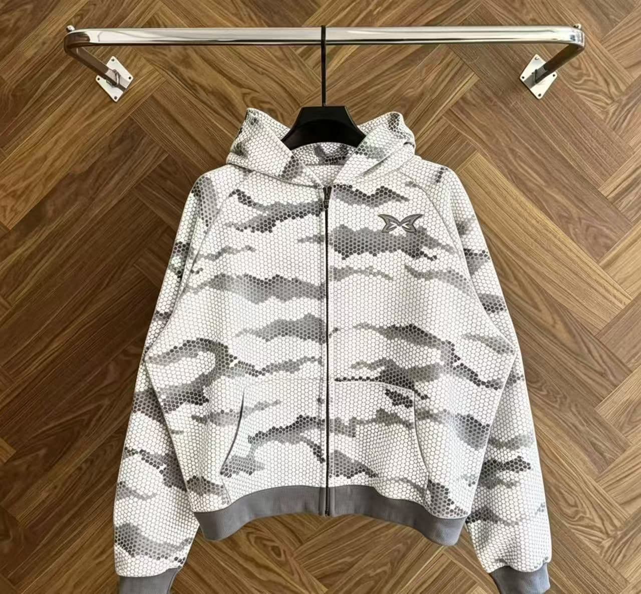White camo mesh zip-up hoodie on hanger against wooden background.