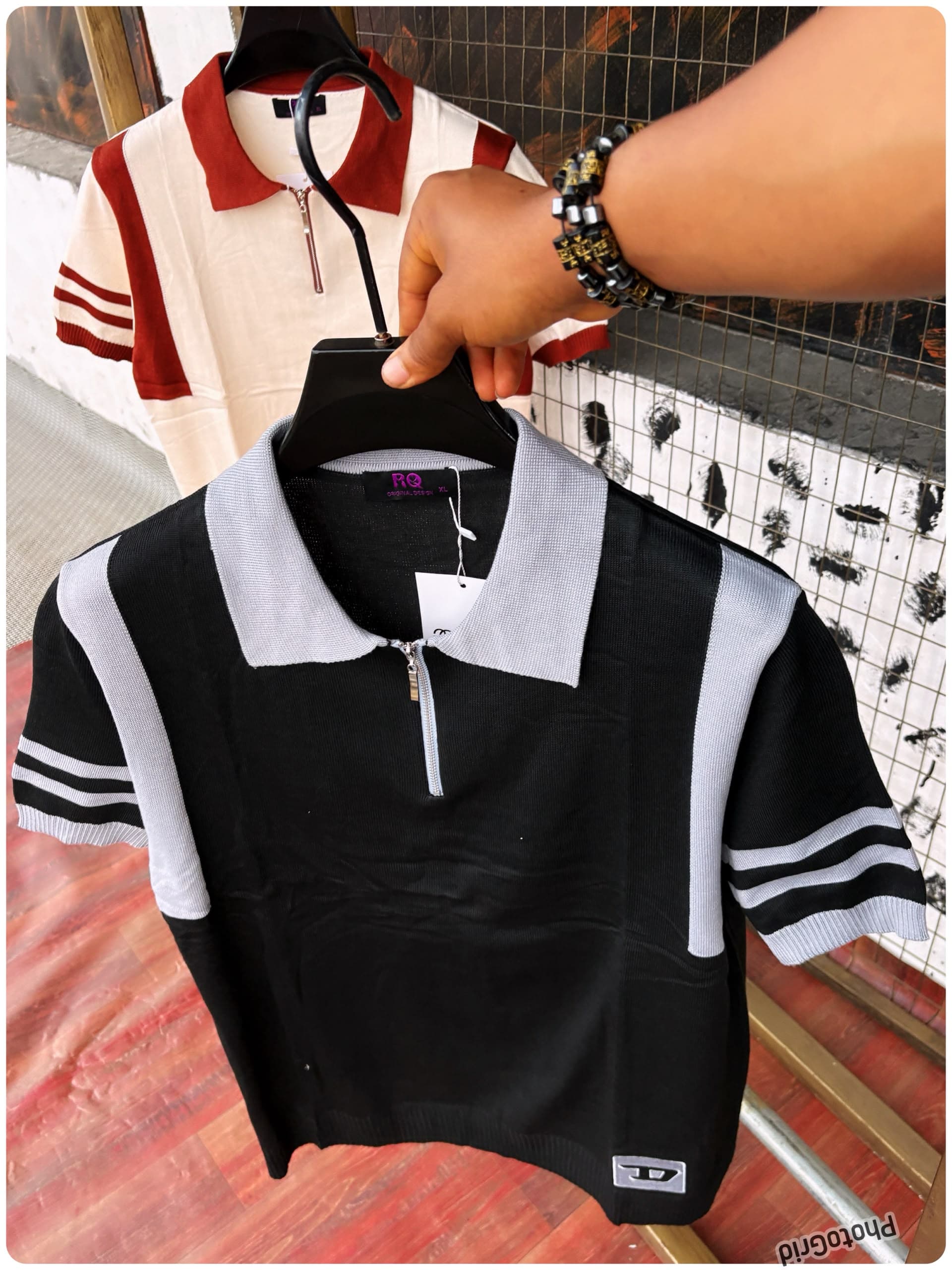 Black and gray colorblock knit polo held in front with white and burgundy version in background.