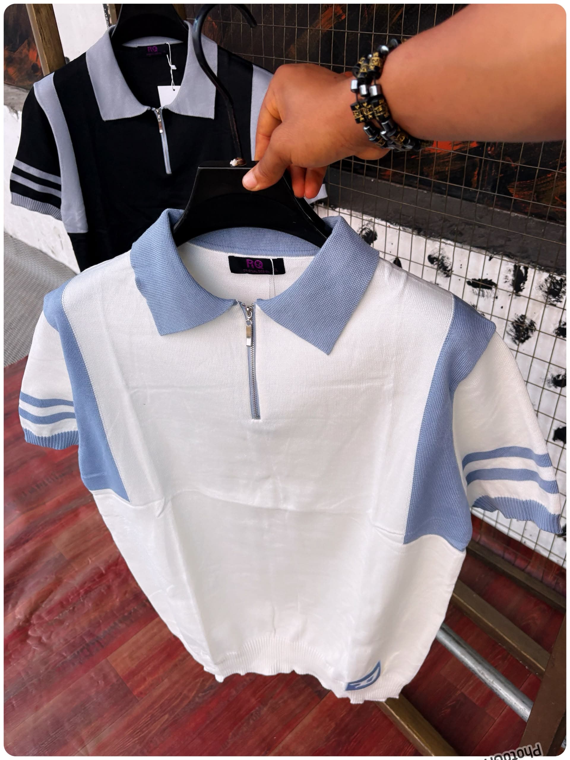 White and light blue colorblock knit polo with striped sleeves in front and black/gray version behind.
