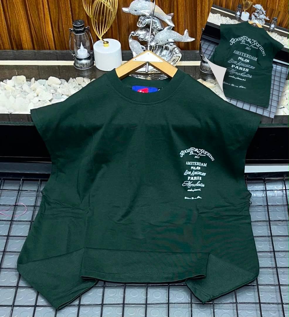 Dark green oversized sleeveless top with white city names graphic on chest.