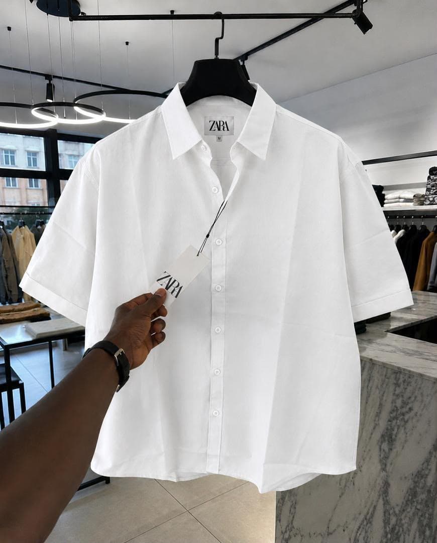 White Zara short sleeve button-up shirt held on a hanger in retail store.