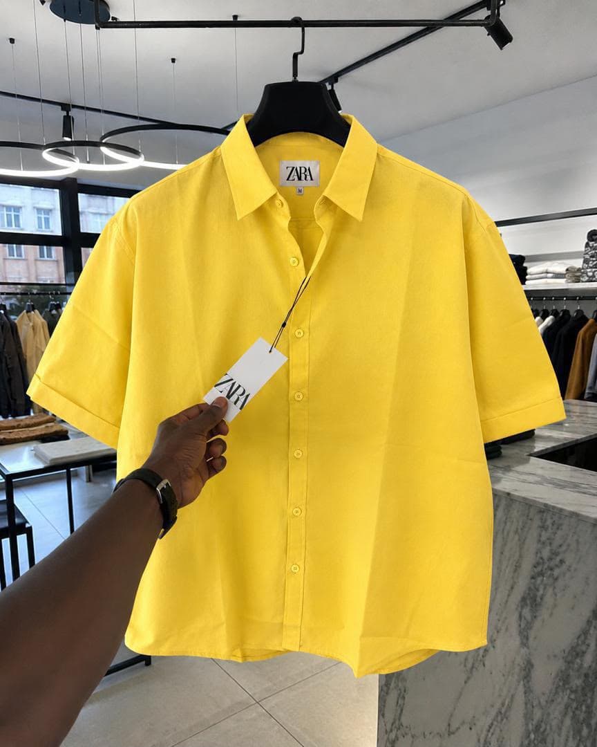 Yellow Zara short sleeve button-up shirt held on a hanger in retail store.