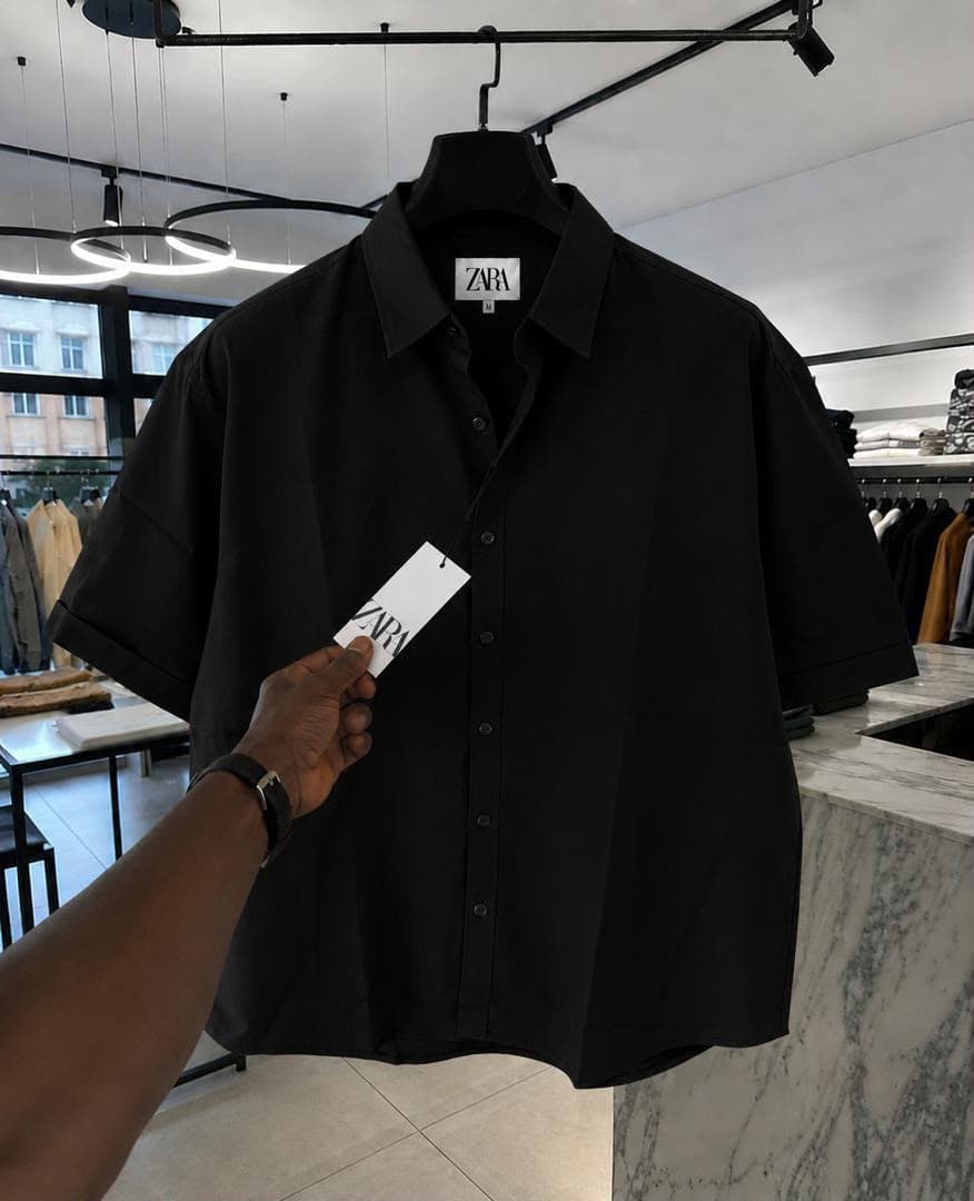 Black Zara short sleeve button-up shirt held on a hanger in retail store.