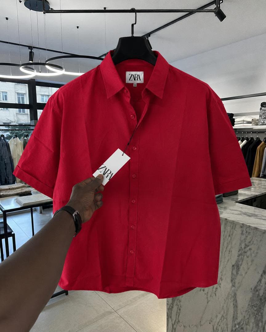 Red Zara short sleeve button-up shirt held on a hanger in retail store.