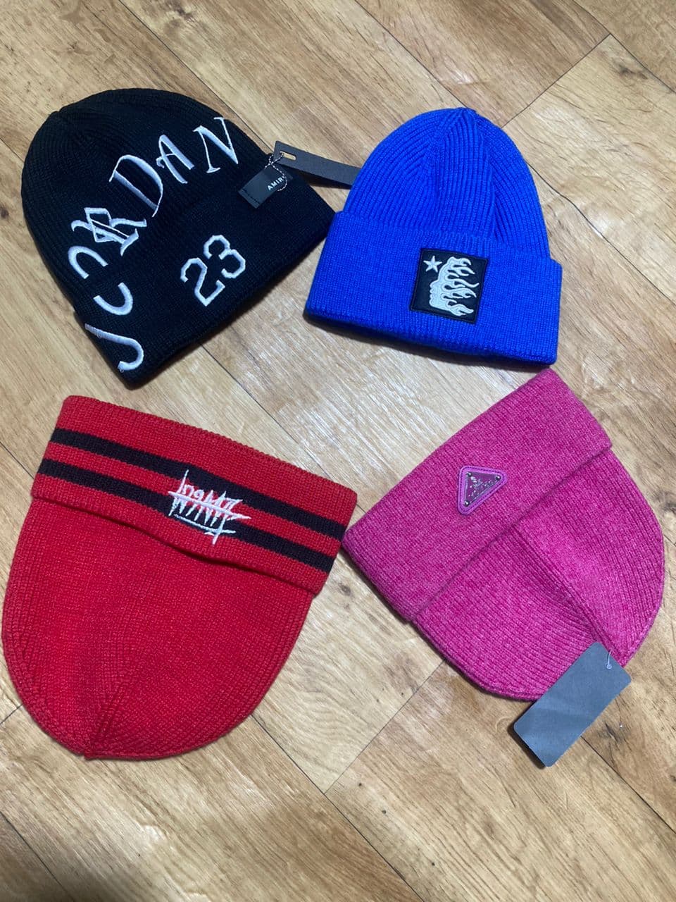 Black Jordan 23 beanie shown alongside blue, red striped, and pink beanies on wooden floor.