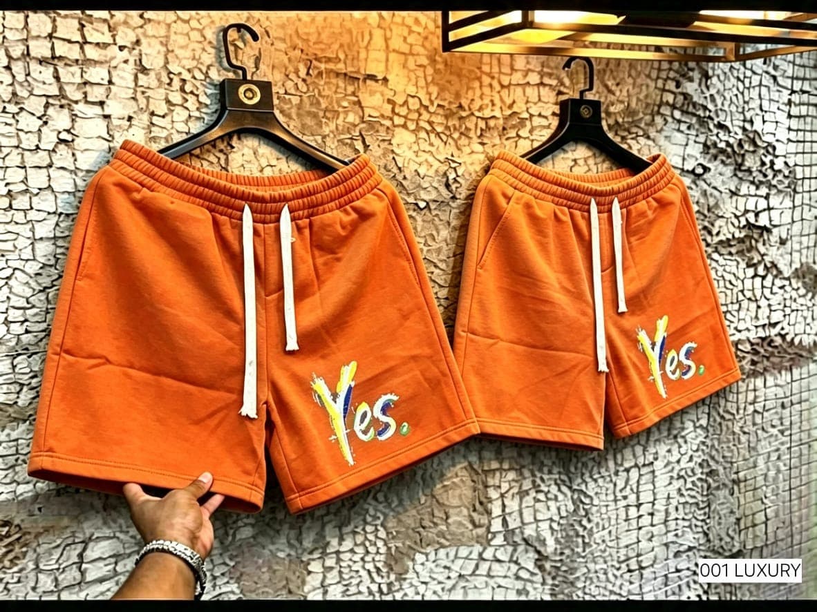 Orange unisex shorts with colorful Yes print shown hanging.