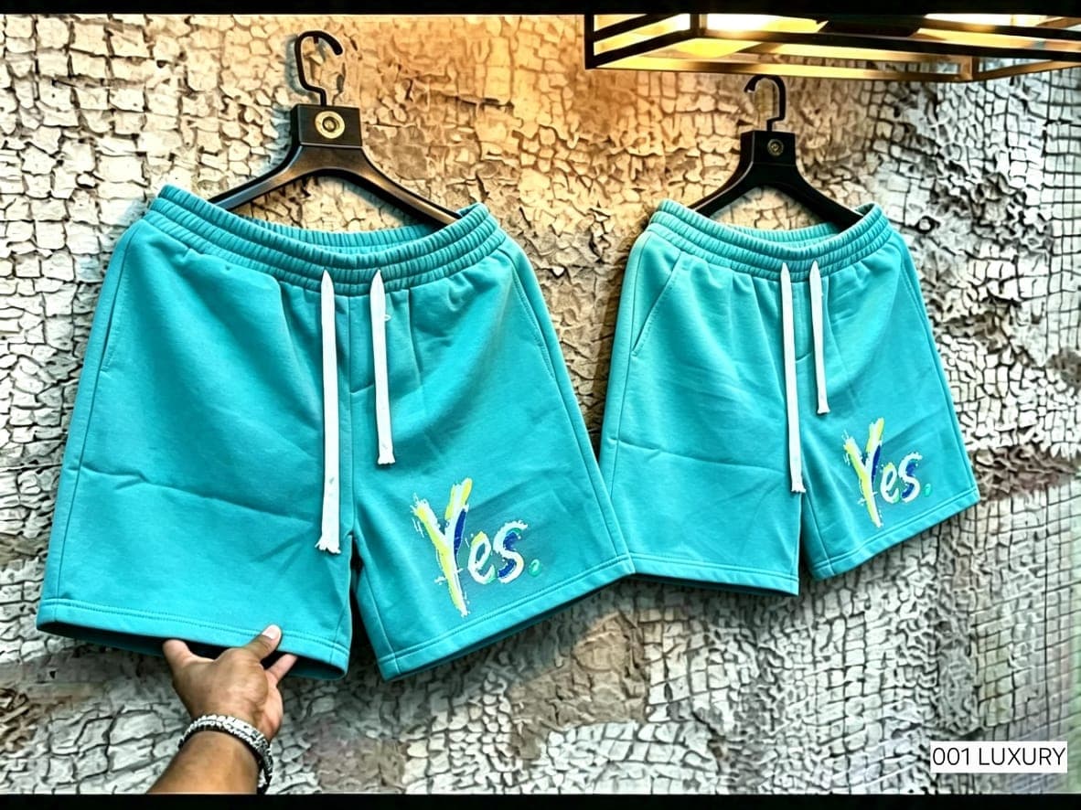 Turquoise shorts with Yes design hanging against textured wall.