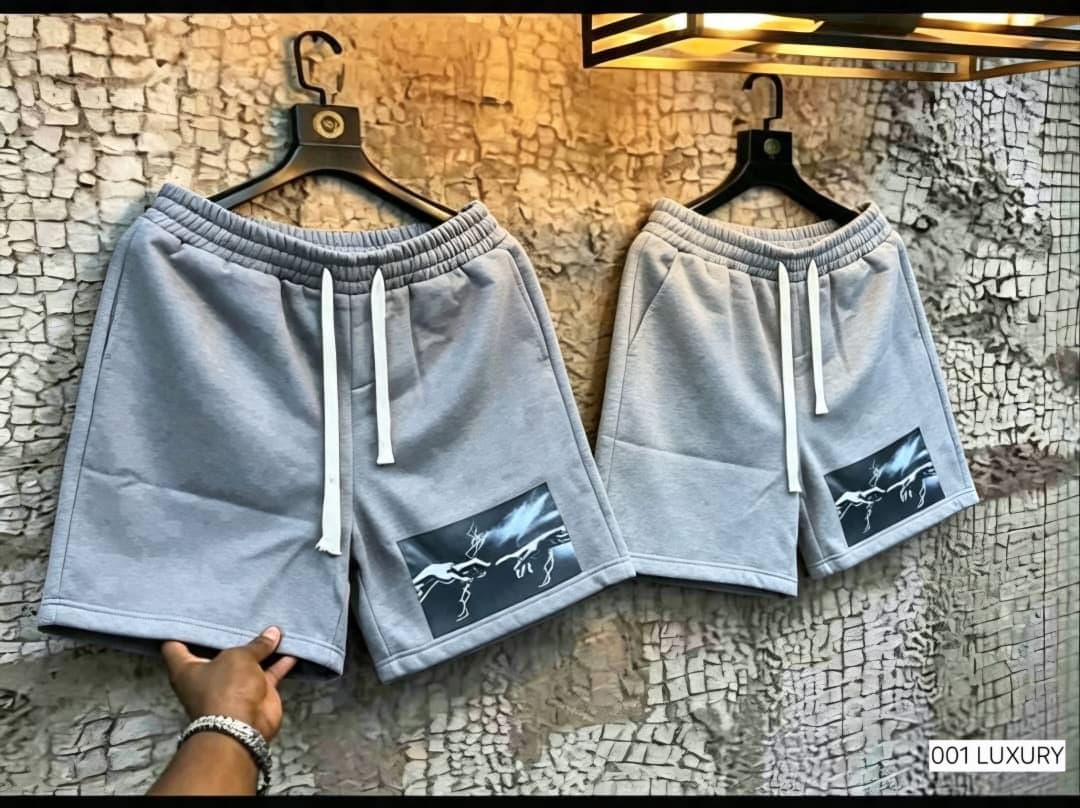 Light gray fleece shorts with hand lightning graphic on the leg, hanging on wall.