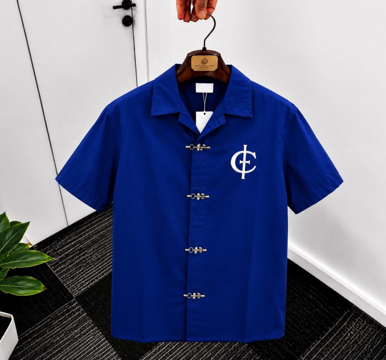 Blue unisex short sleeve shirt with toggle buttons and white chest logo.