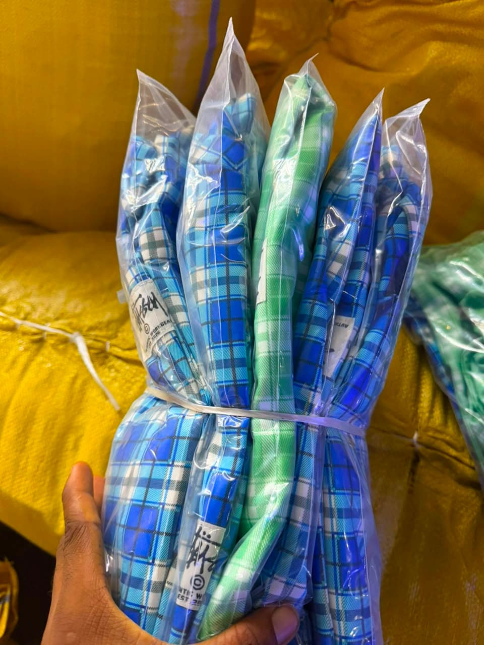 Bundle of packaged Stussy plaid jackets in blue, green, and light green checks.