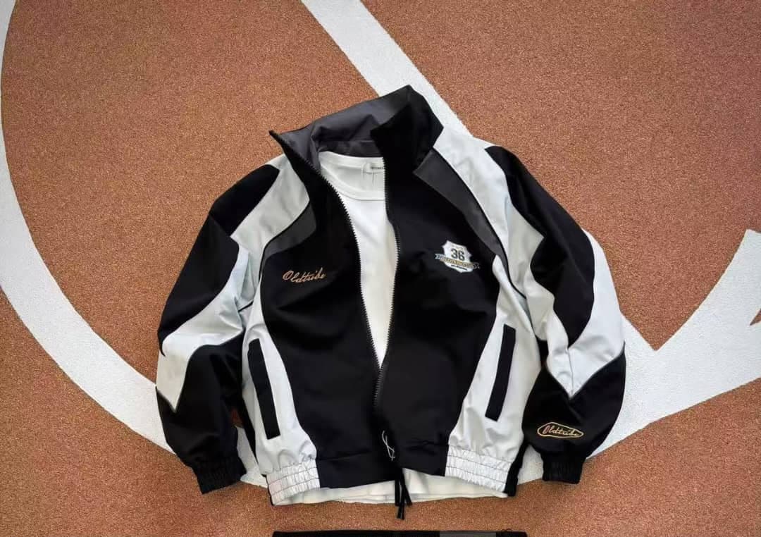 Black and white Oldtribe windbreaker jacket displayed on track surface.