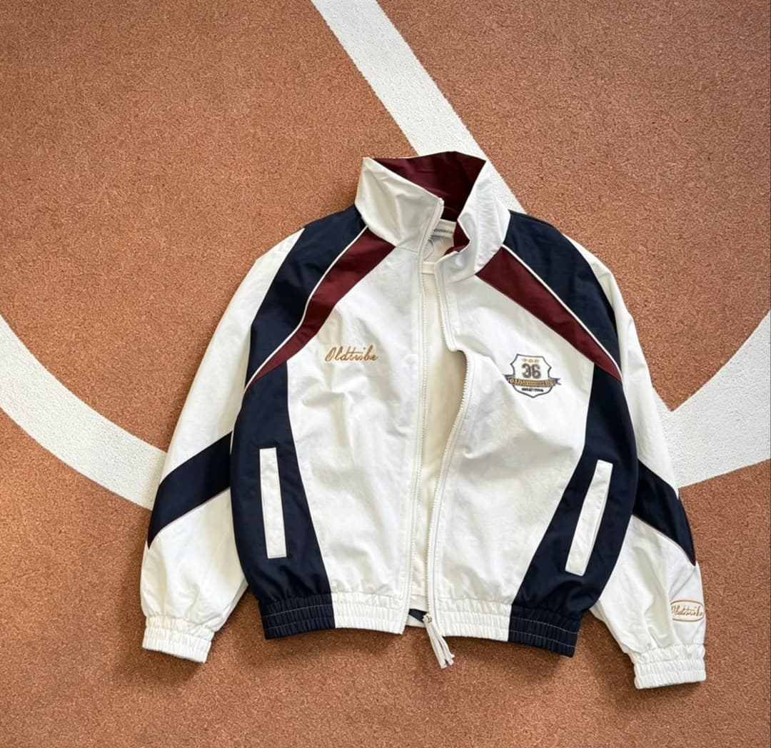 White Oldtribe windbreaker jacket with navy and burgundy panels laid on track surface.