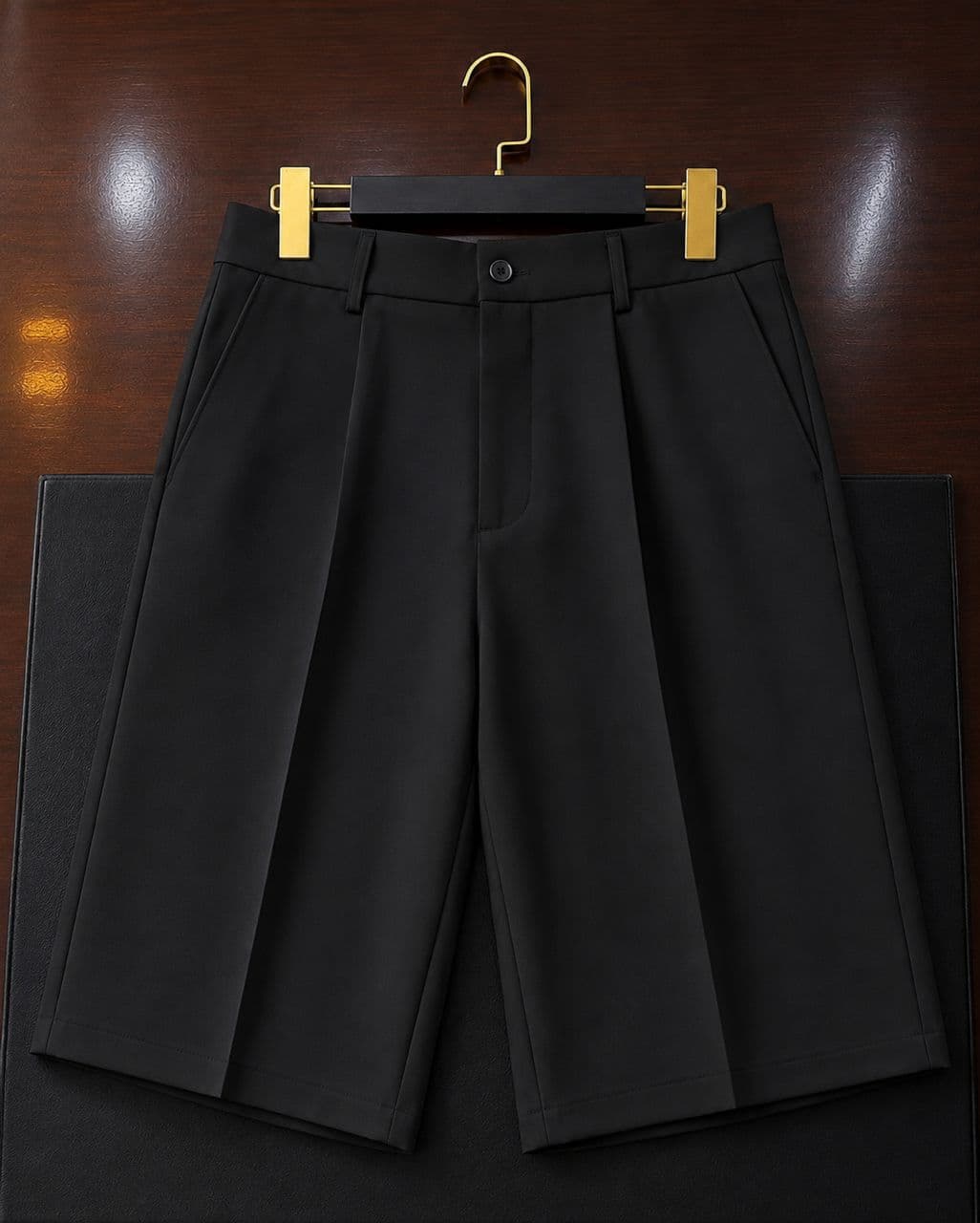 Black tailored pleated shorts flat lay on wooden surface.