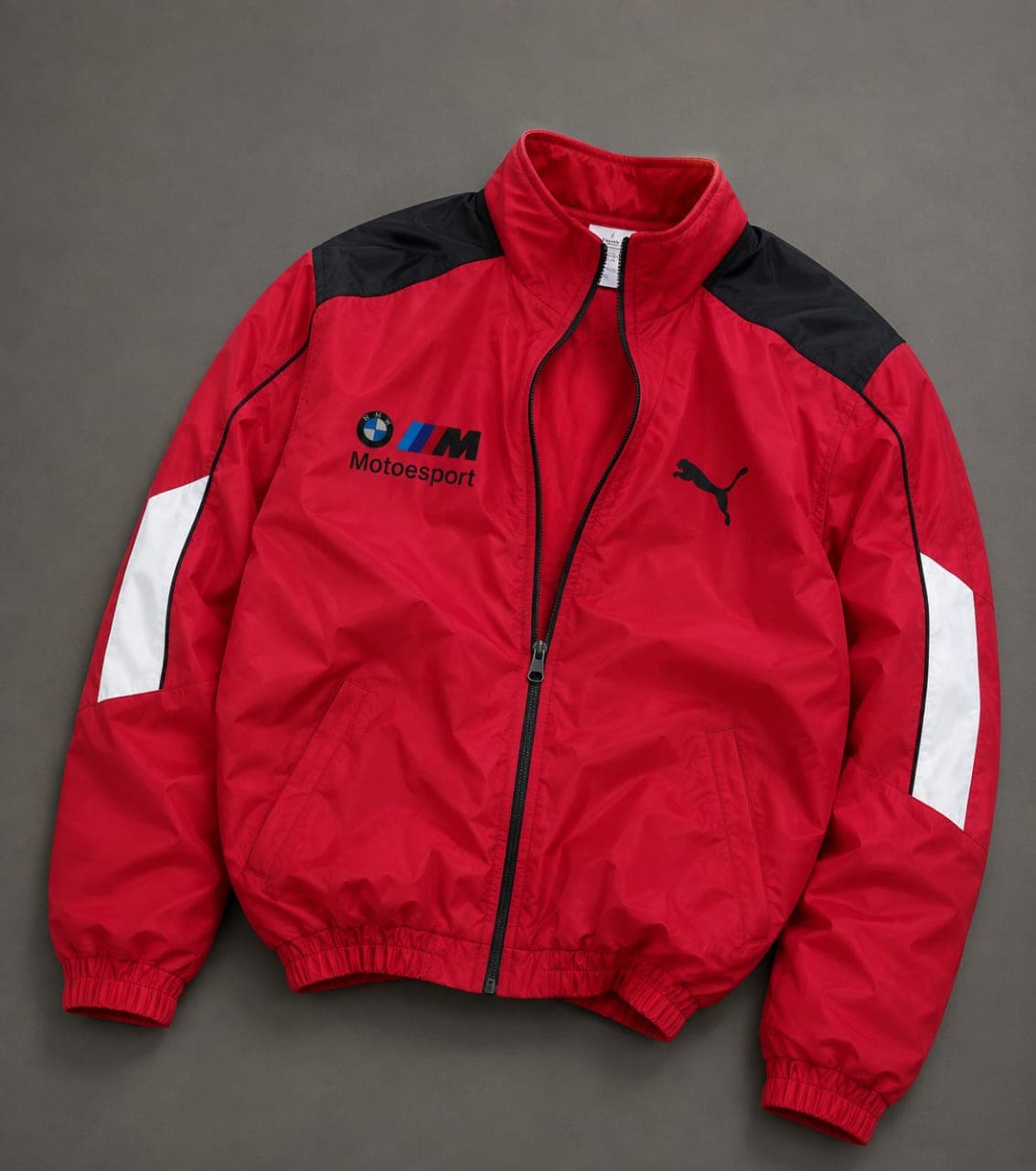 Red Puma BMW M Motorsport track jacket with black shoulders and white sleeve stripes, laid flat.