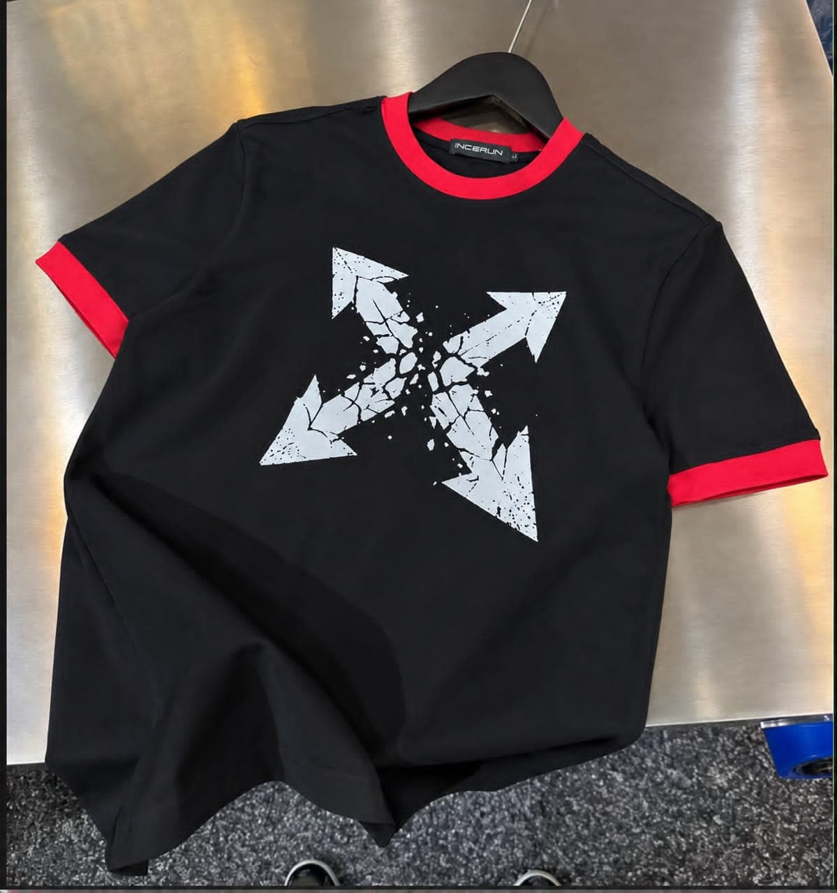 Flat lay of black ringer t-shirt with red trim and large white cracked arrows graphic on front.