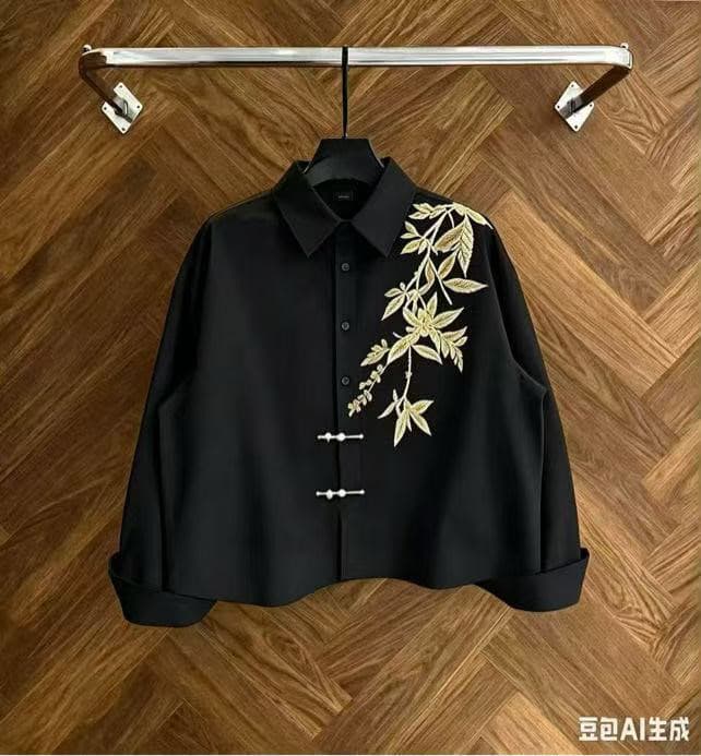 Black cropped button-up shirt with gold leaf embroidery on wooden background.