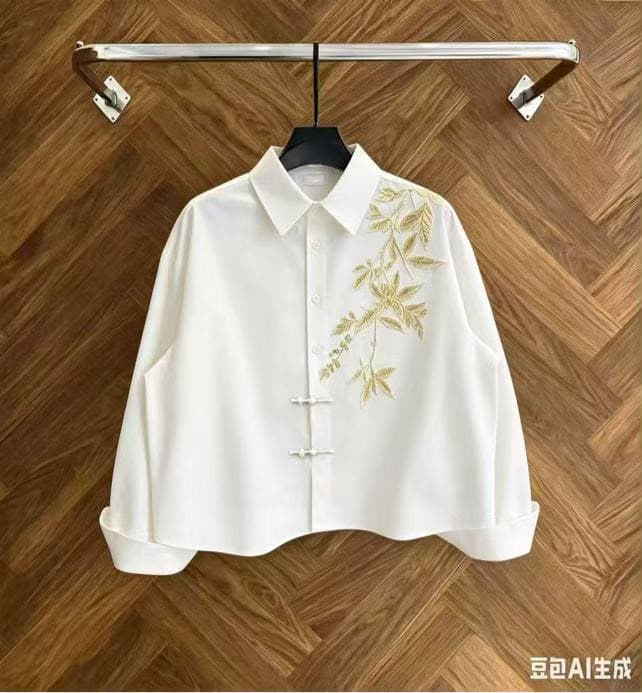 White cropped button-up shirt with gold leaf embroidery on wooden background.