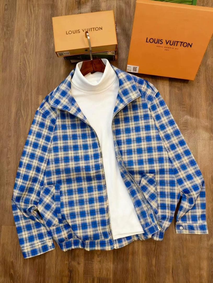 Blue plaid zip-up jacket laid flat on wooden floor, showing back and side profile with elastic waistband and LV boxes in background.