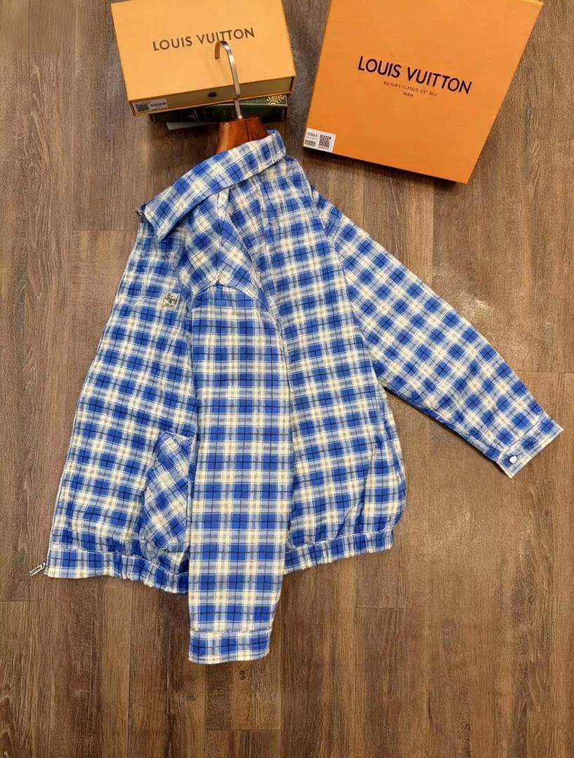 Blue plaid zip-up jacket styled over white turtleneck on wooden floor, front view with zipper open and luxury boxes behind.