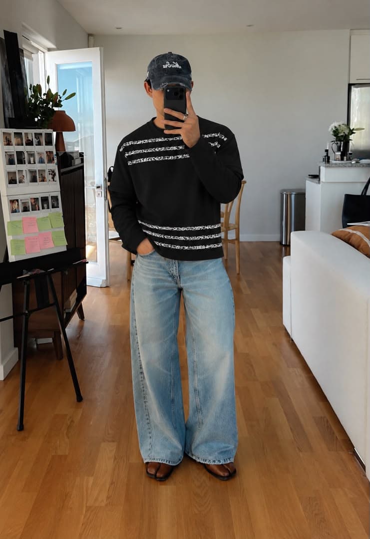 Man wearing the black layered sleeve top with jeans and cap.