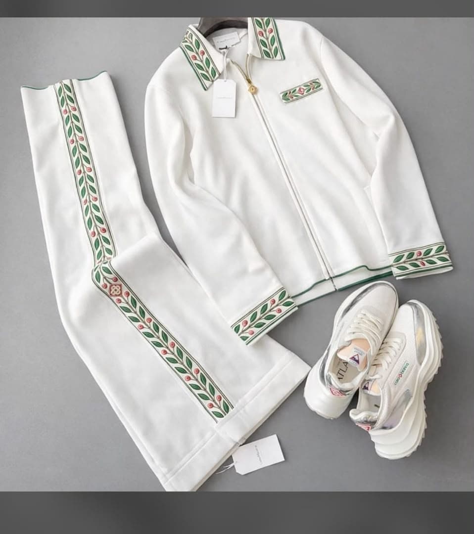 White embroidered tracksuit jacket and pants laid flat alongside white sneakers and tags.