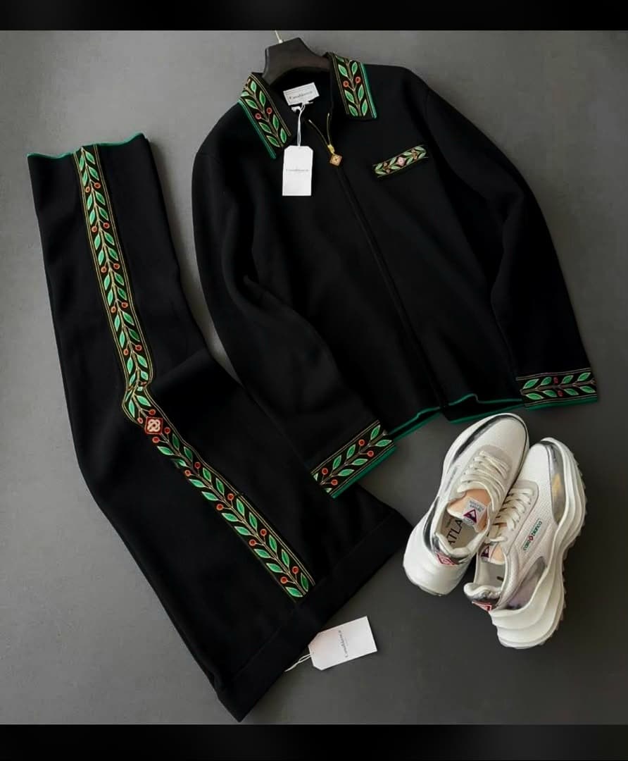 Black embroidered tracksuit jacket and pants laid flat alongside white sneakers and tags.