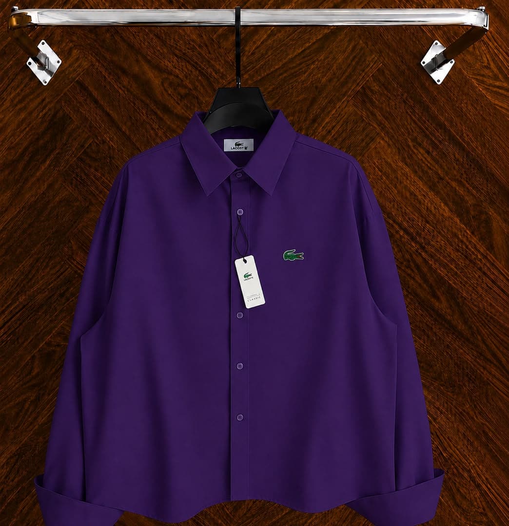 Purple Lacoste long sleeve button-down shirt with green crocodile logo on wooden background.