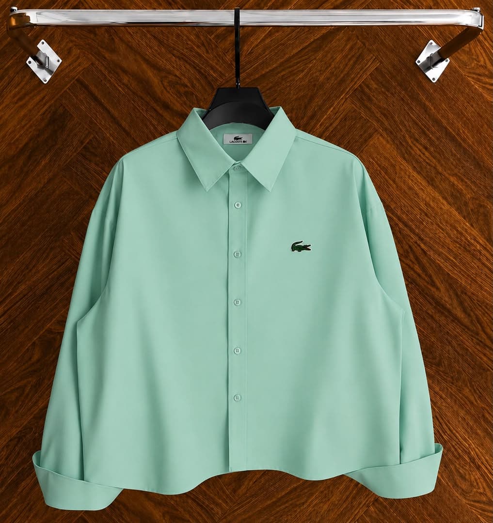 Light green Lacoste long sleeve button-down shirt with logo shown hanging on hanger.