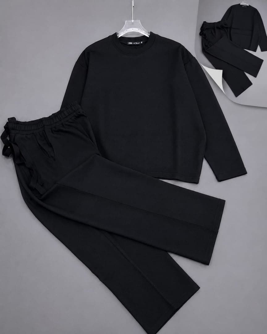 Black textured knit two-piece set with long sleeve top and pants on light background.