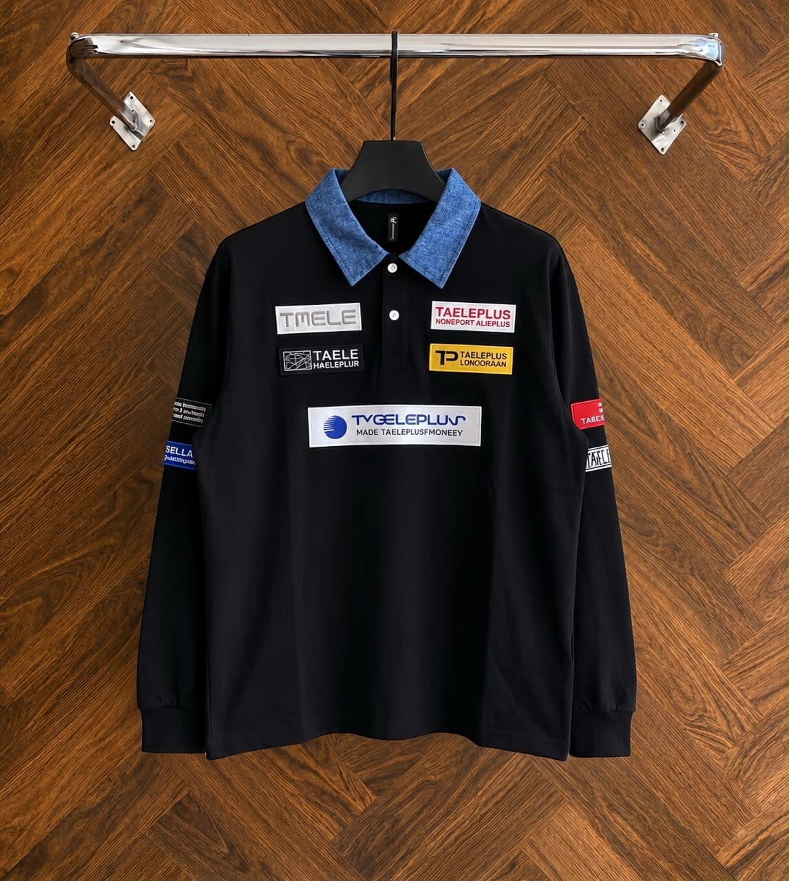 Black long sleeve polo with denim collar and multiple patches on wooden hanger.