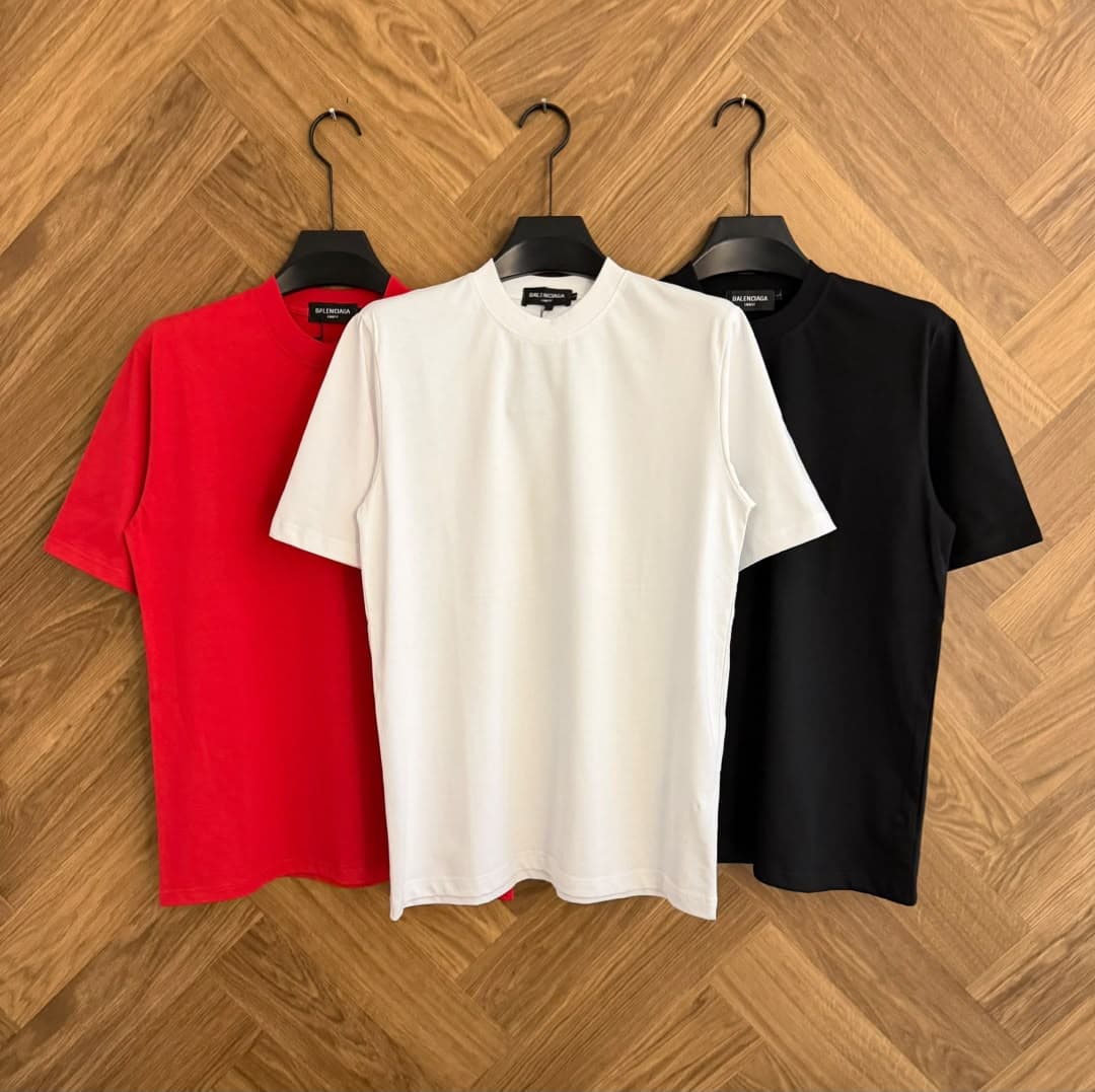 Red, white and black plain t-shirts hanging side by side on wood floor.