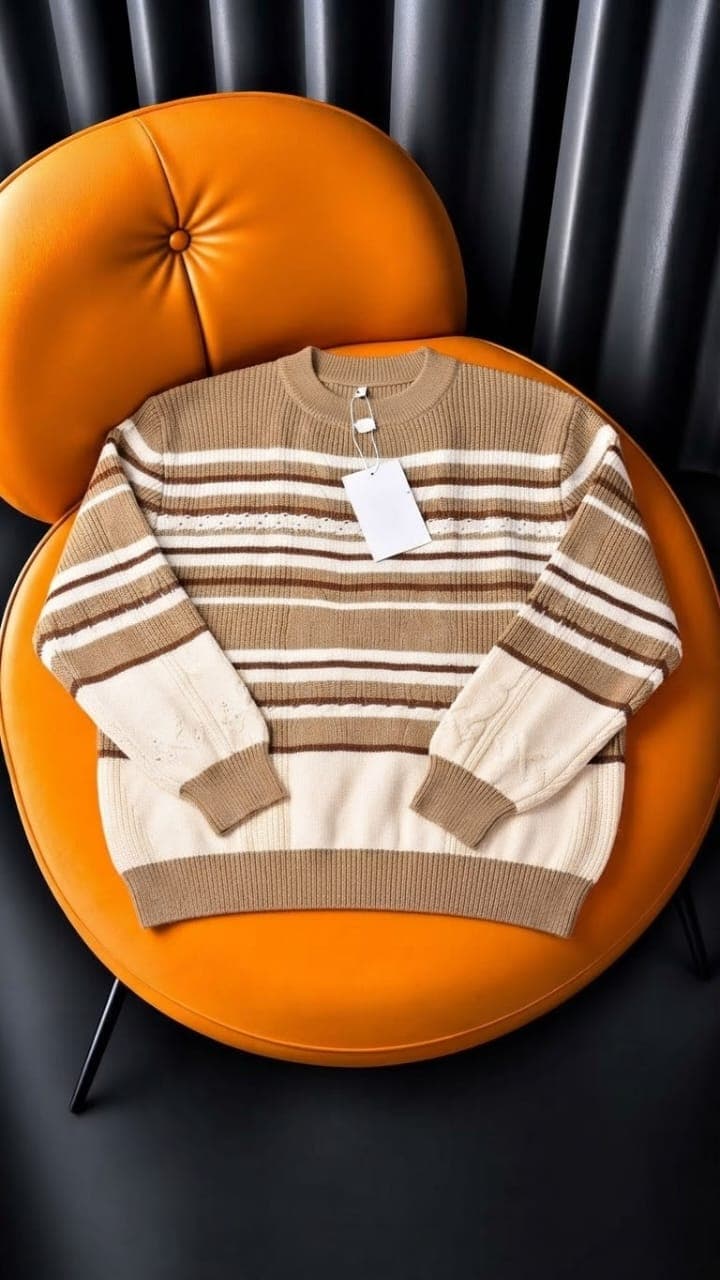 Cream brown black striped cable knit sweater displayed on orange chair.