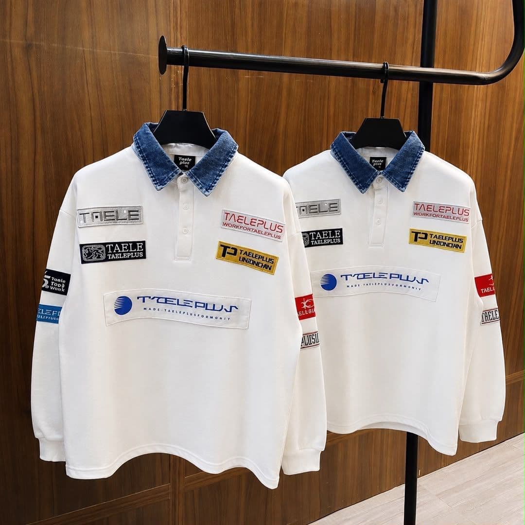 White long sleeve polo with denim collar and multiple chest patches on wooden hanger.