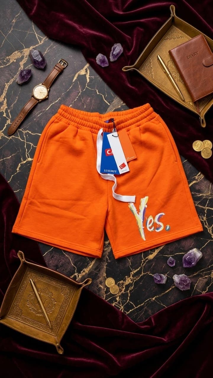 Orange fleece shorts with colorful Yes graphic on dark velvet with crystals and watch.