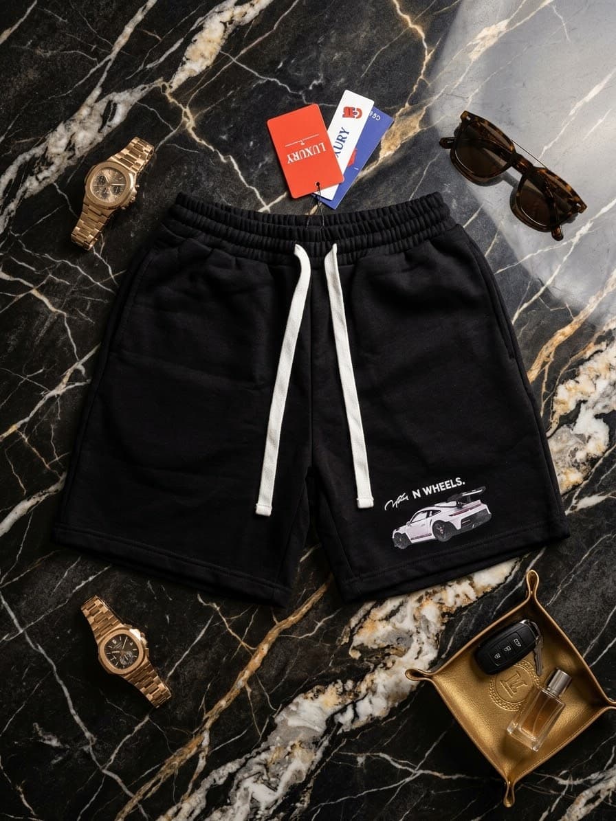 Black fleece shorts with white car graphic and ON WHEELS text on marble with sunglasses and tray.