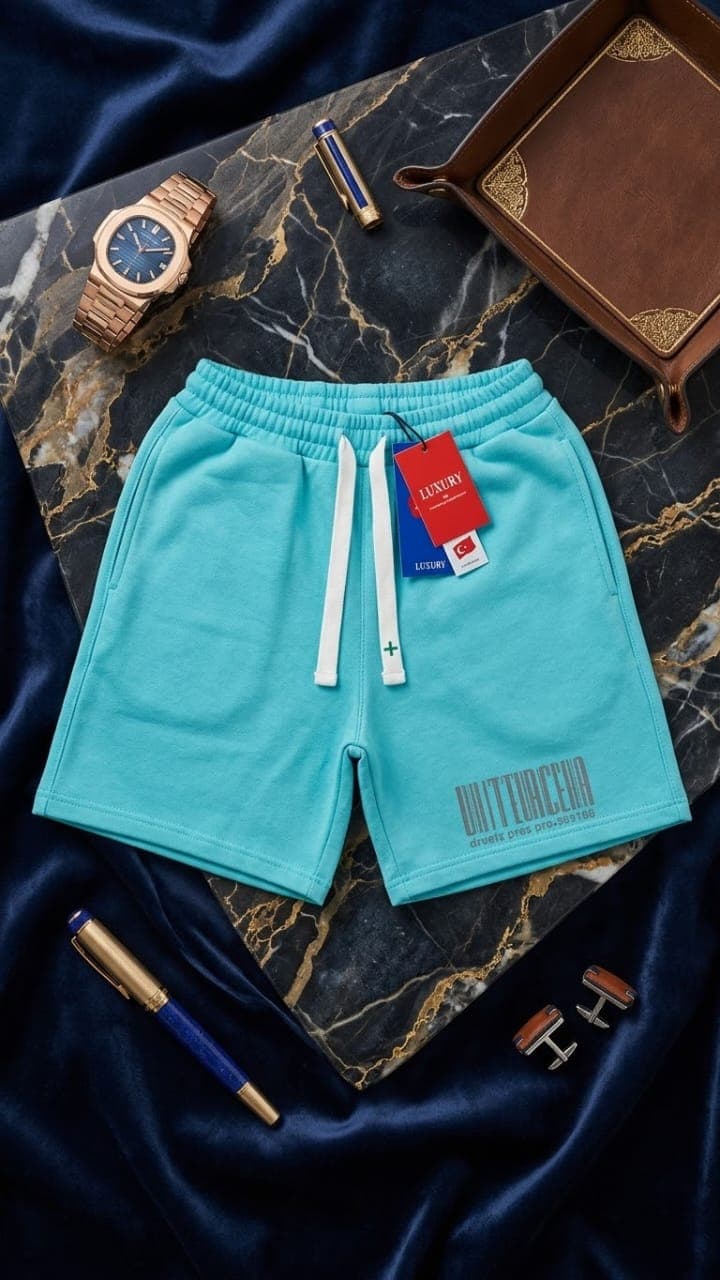 Turquoise fleece shorts with large block text graphic on marble surface with pen and cufflinks.