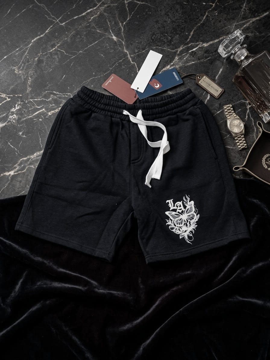 Black fleece shorts with white butterfly graphic on dark velvet and marble background with watch.