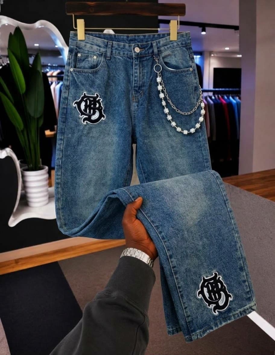 Red denim jeans with black script text on leg, shown on hanger and held by hand.