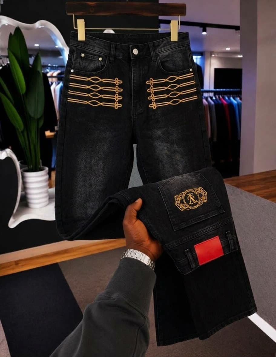 Black baggy jeans with metal clasps and distressing, held by hand to show wide leg flare in retail setting.