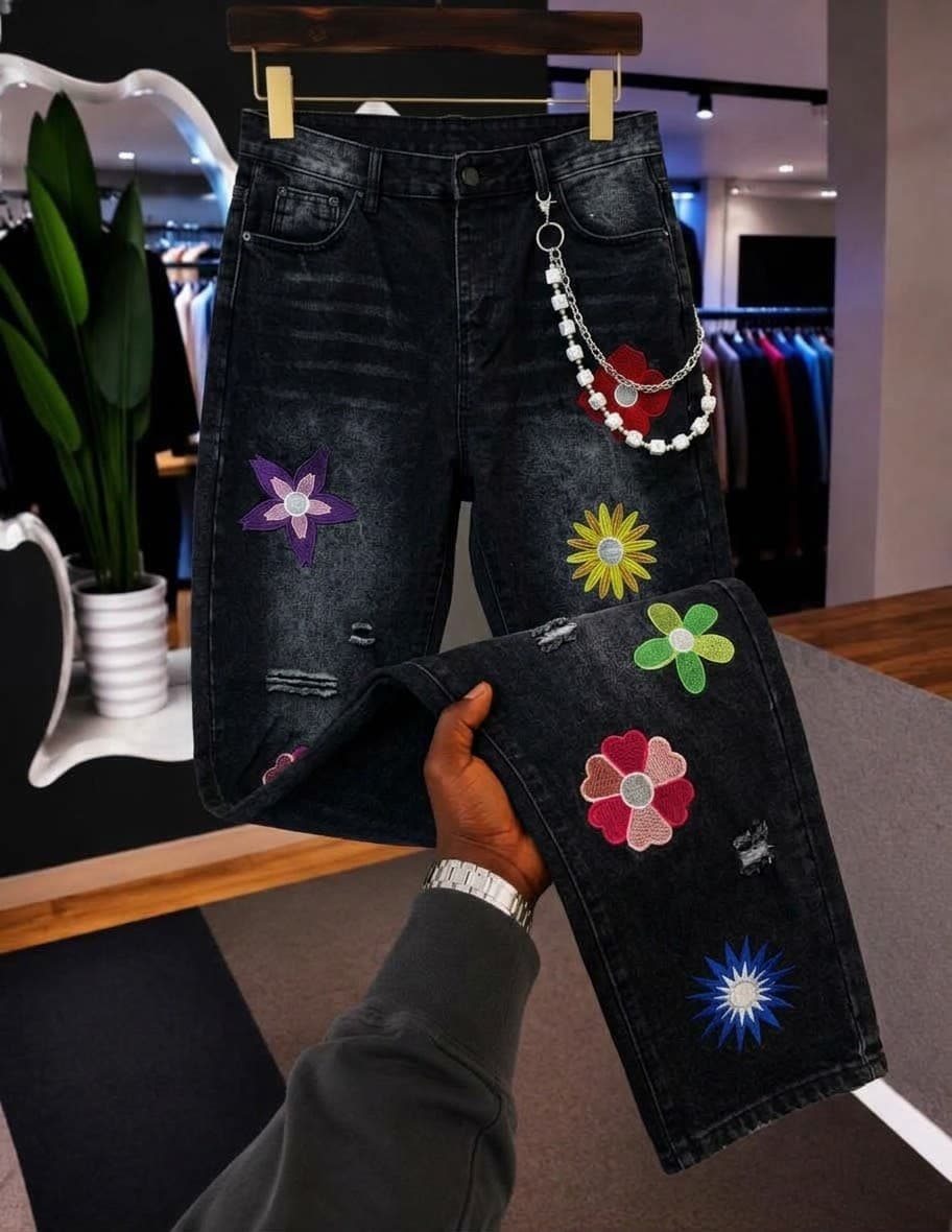 Black jeans with colorful flower embroidery patches, beaded chain and distressing, held to display details.