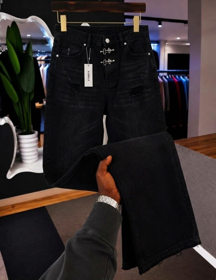Black jeans with gold chain embroidery on pockets and ornate back pocket design with red patch, held to show details.