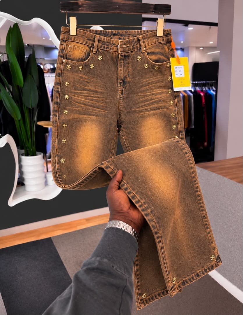 Flat lay of black baggy jeans with silver chain, cross pendant and metal clasps on grey carpet.